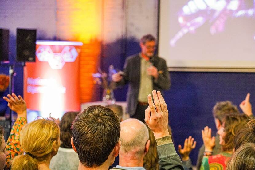 Deelnemers steken de handen op bij de presentatie